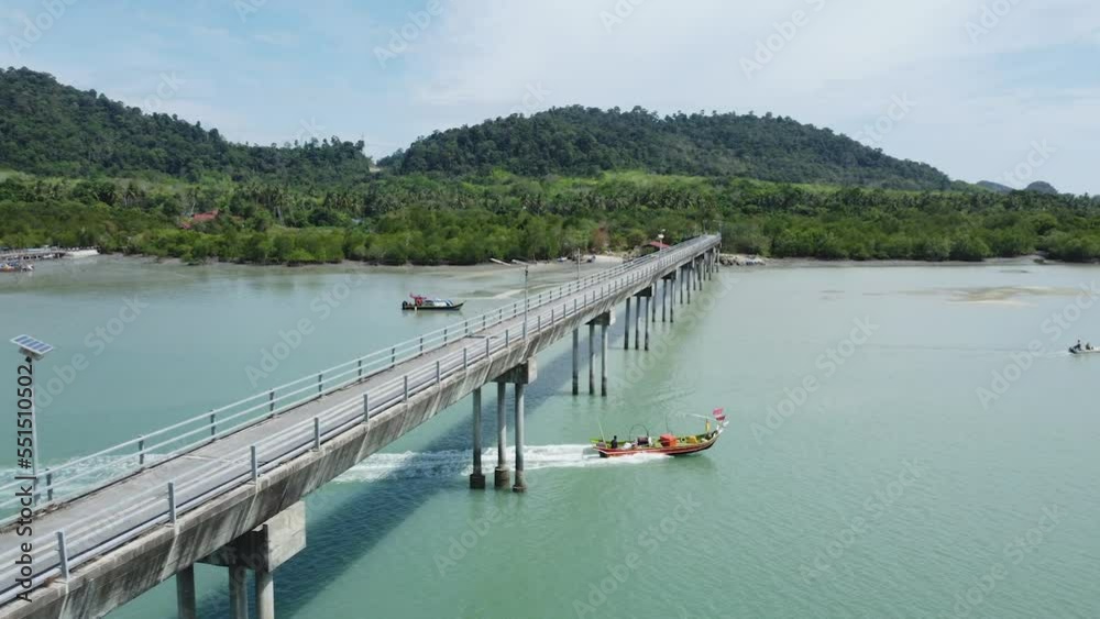 Boat goes under a long bridge on tropical island with turquoise water, Langkawi Boat goes under a long bridge on tropical island with turquoise water, Langkawi