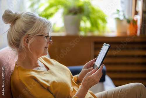 Senior woman using e-reader and reading an e-book at home
 photo