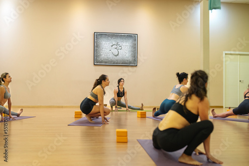 Latin teacher teaching a yoga class with the Ardha malasana posture.