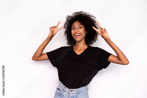 Portrait of cheerful young woman making peace gesture against white background. African American lady wearing black T-shirt and jeans expressing happiness and joy. Success and happiness concept