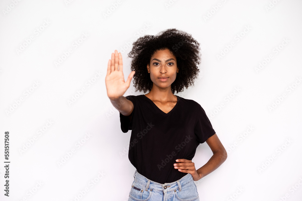 Portrait of confident young woman making stop gesture over white background. African American lady wearing black T-shirt and jeans showing warning sign. Forbiddance concept Portrait of confident young woman making stop gesture over white background. African American lady wearing black T-shirt and jeans showing warning sign. Forbiddance concept