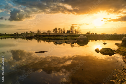 Sunset landscape in the natural monument of Los Barruecos de Caceres. The clouds surround the sun reflected in the water of the lagoon. photo