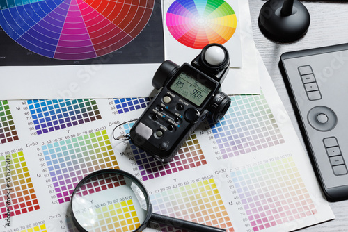 Photographer's desk. Graphic tablet, flashmeter, magnifier, printouts of color wheels and CMYK color samples. View from above. photo