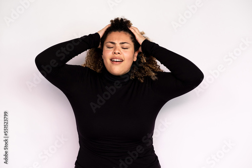 Tired young woman suffering from headache. Female African American model with curly hair and closed eyes in casual clothes holding hands on her head because of headache. Fatigue, pain concept © KAMPUS
