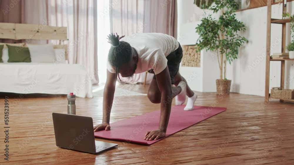 Young Beginer African American man doing cardio exercise on floor in living room. Attractive handsome sport male spend leisure activity time to workout for healthcare by follow online instruction on