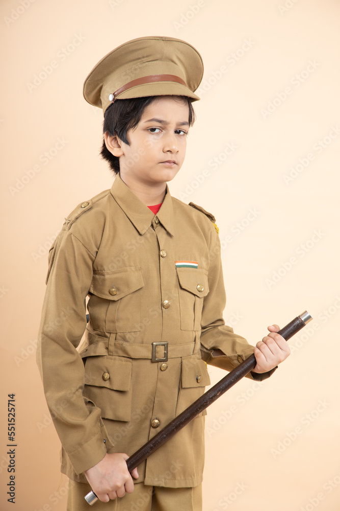 Indian boy child wearing police uniform showing with his nightstick in hand isolated on beige studio background. Indian boy child wearing police uniform showing with his nightstick in hand isolated on beige studio background.