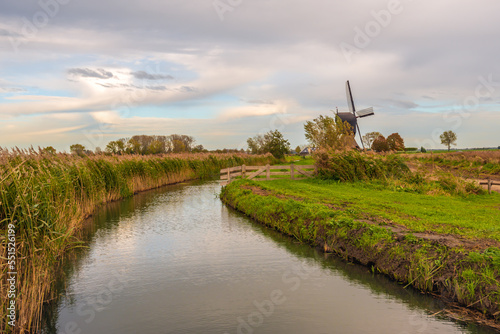 Polder landscape with a curved  recently cleaned ditch and a historic windmill in the background. On one side of the ditch the reeds already are yellowing due to the seasonal change to autumn.