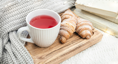 A cup of red tea, a croissant and a knitted element on a wooden tray.