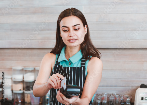 An image of a female shop owner barista Hand holding credit card and payment terminal at coffee shop