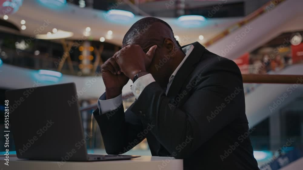 Middle-aged African businessman worker entrepreneur with laptop sad upset feel headache pain ache trouble with computer work adult man has problem anxiety with online app crash application bad news