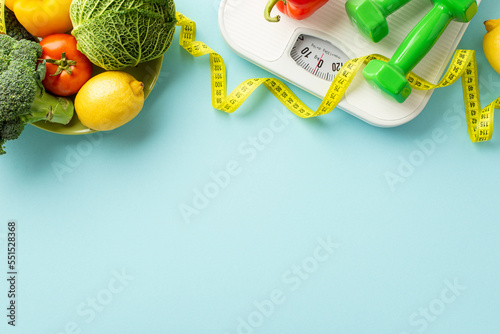 Slimming concept. Top view photo of plate with vegetables cabbage lemons cauliflower tomato dumbbells scales and tape measure on isolated pastel blue background with copyspace