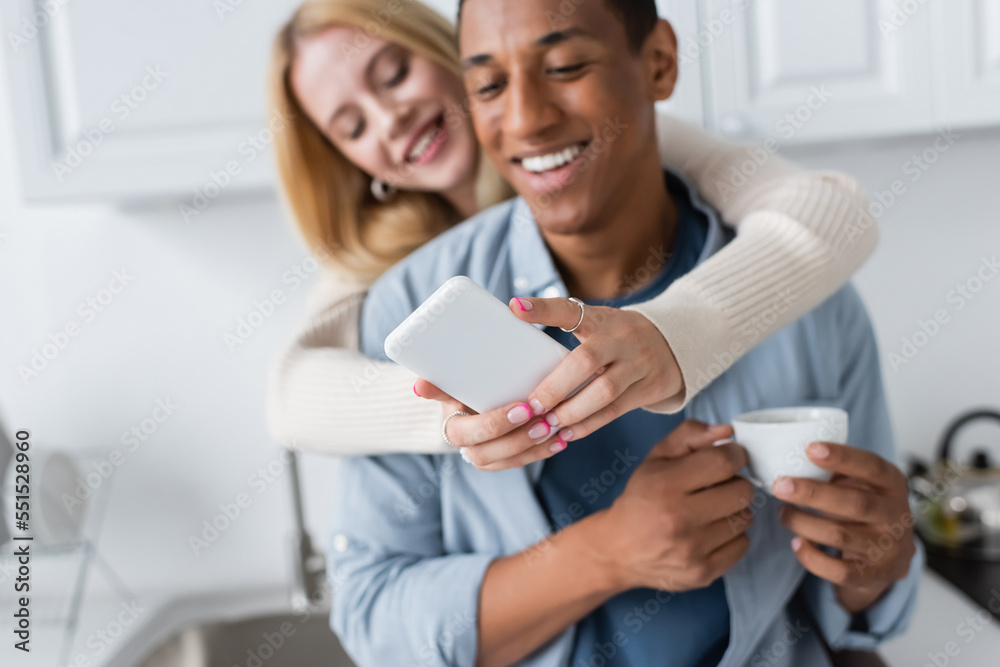 selective focus of smartphone in hands of blurred woman near african american man with coffee cup