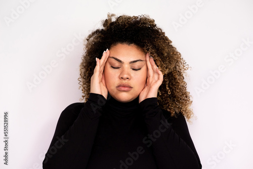 Overworked young woman suffering from headache. Female African American model with curly hair and closed eyes in black turtleneck holding palms at temples because of headache. Tiredness, pain concept © KAMPUS