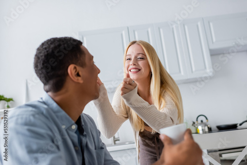 cheerful blonde woman smiling near african american boyfriend in kitchen