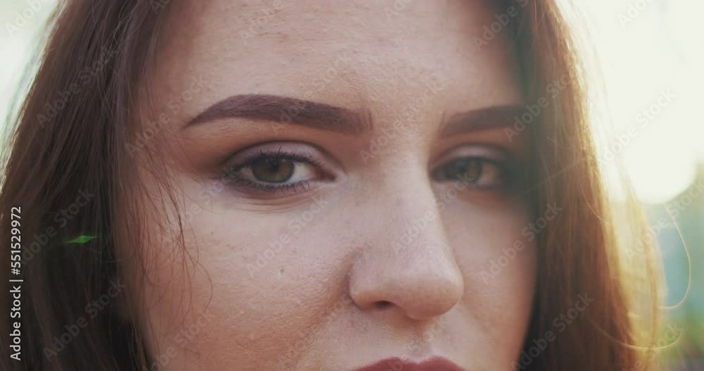 Close up of face of beautiful young Caucasian woman looking straight to camera outdoor. Eyes and smile of happy female smiling. Expressing Emotions concept. Cheerful mood. Charming. Close up of face of beautiful young Caucasian woman looking straight to camera outdoor. Eyes and smile of happy female smiling. Expressing Emotions concept. Cheerful mood. Charming.
