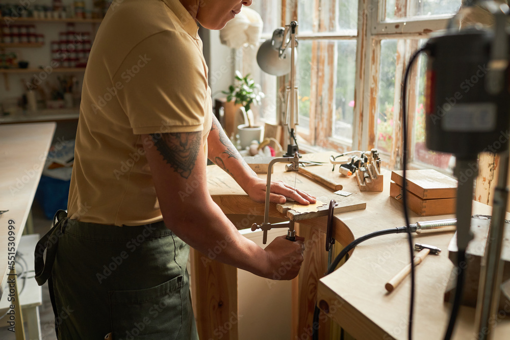 Side view of tattooed artist cutting wood while creating handmade pieces in workshop