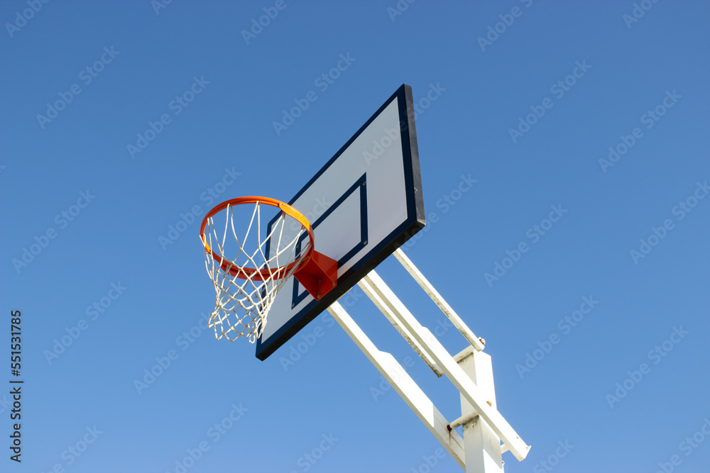 Low angle shot of basketball hoop on sunny day outside at basketball court in city park. Basketball basket with white backboard against blue cloudless sky. Achievement, sports concept