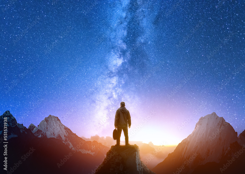 Silhouette of confident man standing on top of mountain with night sky and bright sunset light in background.