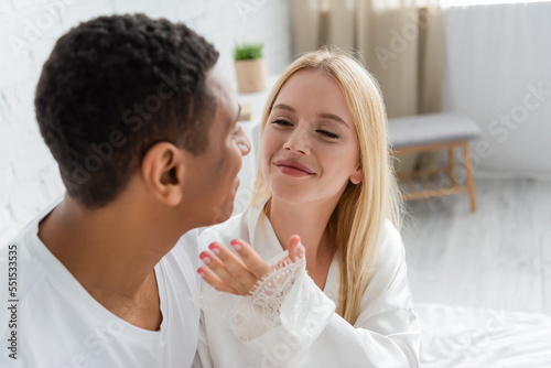 happy young woman holding hand near blurred african american man in bedroom