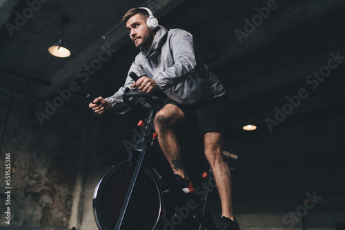 Cheerful man bicycling with headphones in dark room