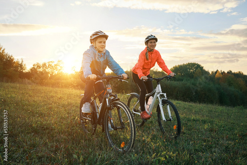 Mother and son ride a bike. Happy cute boy in helmet learn to riding a bike in park on green meadow in autumn day at sunset time. Family weekend. 4K video, Slow motion