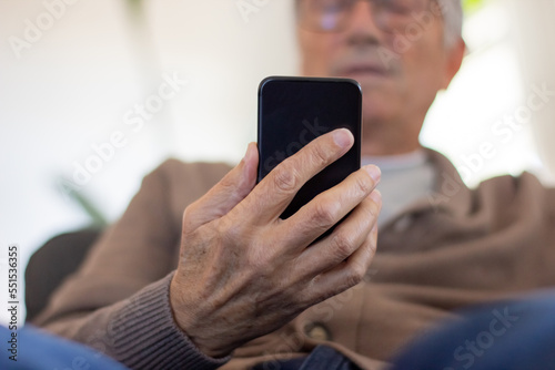 Closeup of man using smartphone. Below view of senior man in cardigan checking message on smartphone. Gadget concept