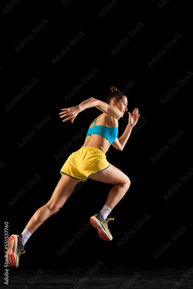 Back view. Sportive muscled woman, professional runner running away isolated on black background. Sport, fitness, competition, speed and ad