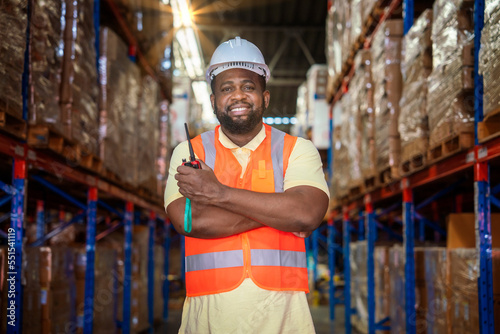 African american black worker in reflective suit, helmet, holding walkie talkie standing with crossed arms crossed in warehouse, distribution center.