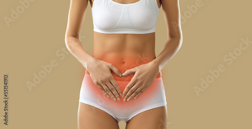 Girl suffering from severe period cramps. Woman in underwear having acute menstrual pain standing on beige background holding hands on red inflamed stomach, cropped shot, banner. Menstruation concept