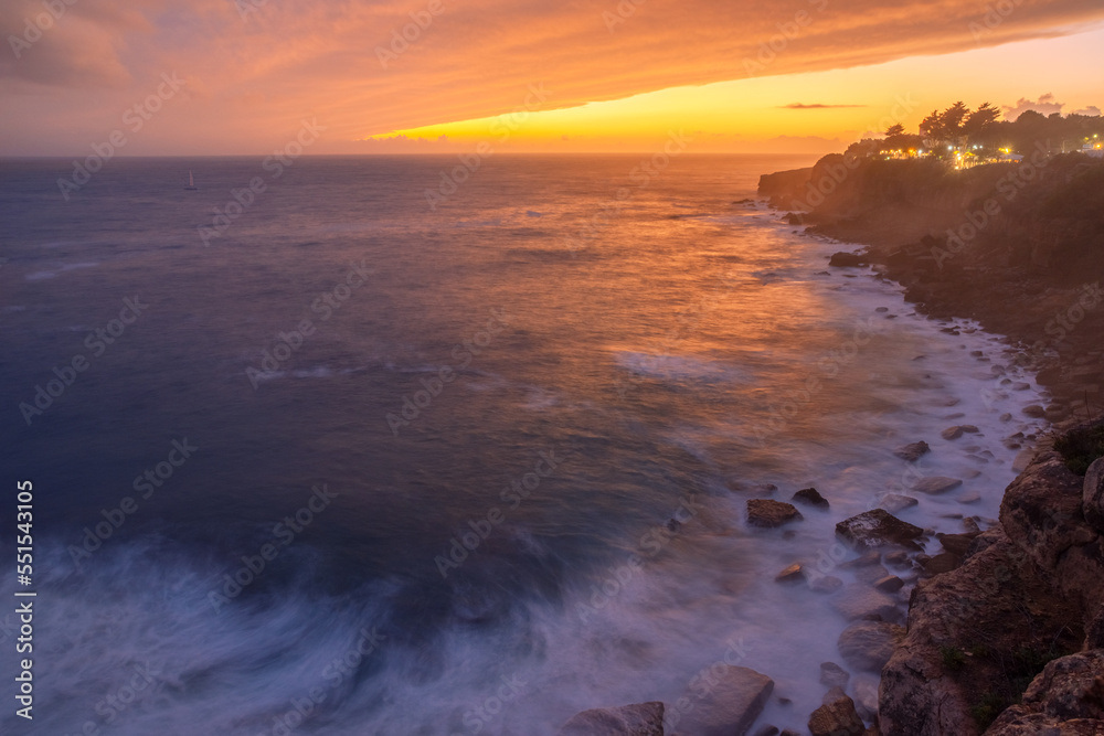 Obraz premium Red colorful sunset and vivid dramatic sky at rocky shore of the Atlantic ocean.