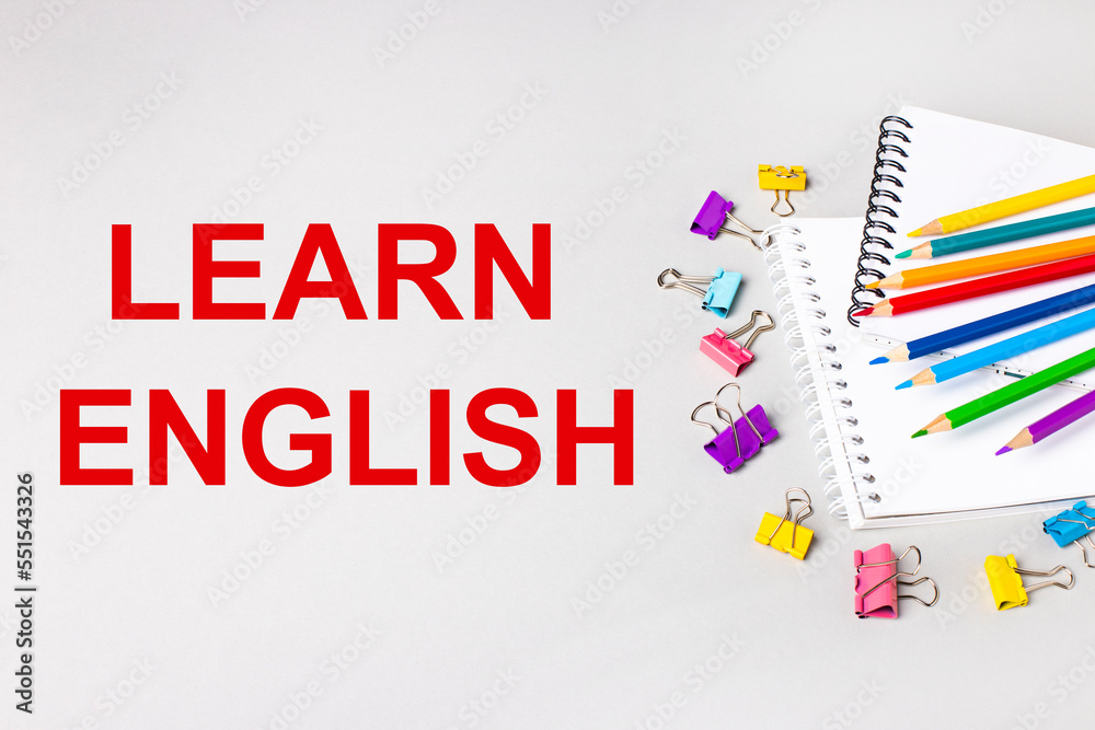 Notebooks, colored pencils and paper clips on a light gray table. The inscription LEARN ENGLISH. Banner
