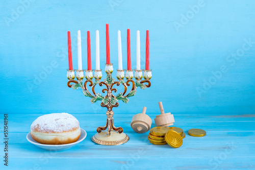 Menorah, candles, chocolate coins, spinning tops for Jewish holiday Hanukkah on blue wooden background.