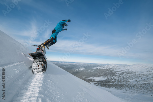 Snowbike rider jumping on steep snowy slope. Modify motorcycle with ski and special snowmobile-style track instead of wheels photo