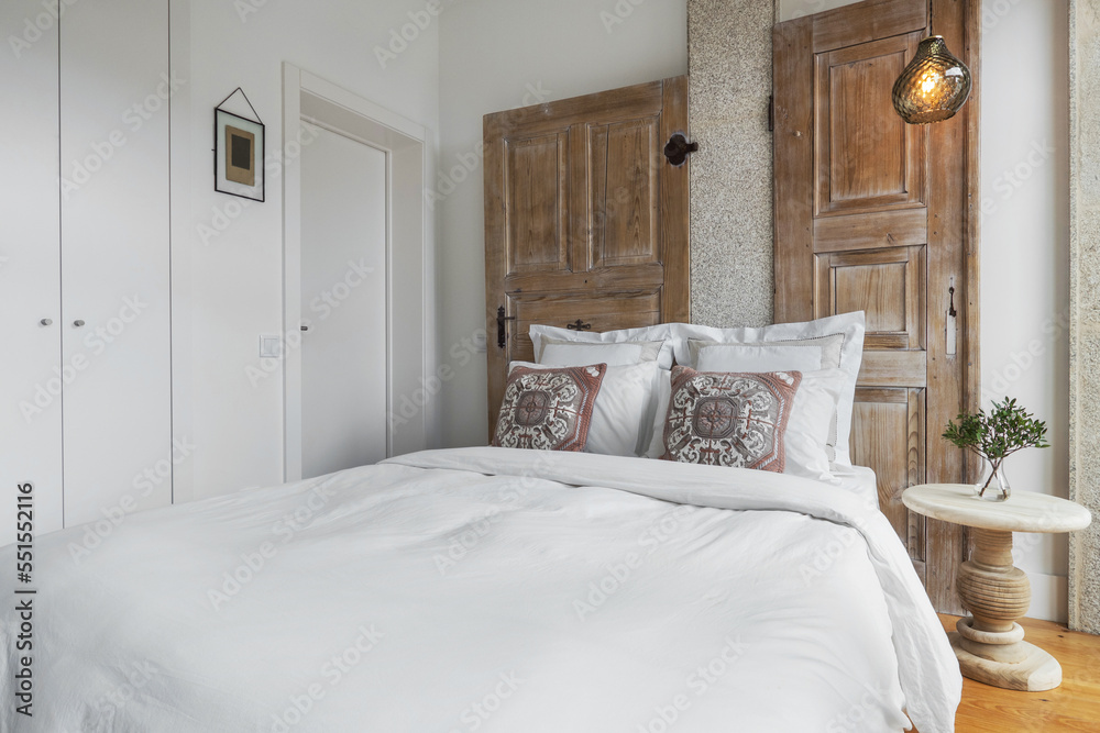 Bright bedroom interior design. Double bed with white linens, white walls and wooden doors as decor Bright bedroom interior design. Double bed with white linens, white walls and wooden doors as decor