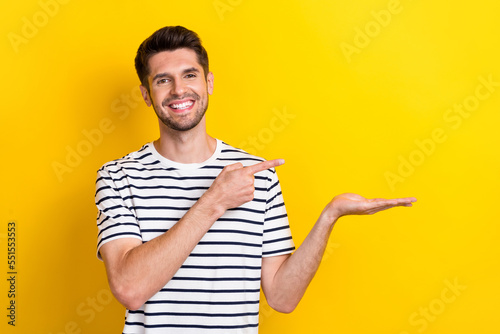 Photo of glad positive smile business man wear striped t-shirt hold palm finger direct empty space novelty news isolated on yellow color background photo