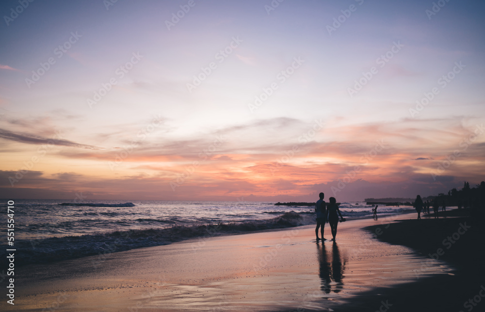 Silhouette of people walking along sandy beach in sunset time