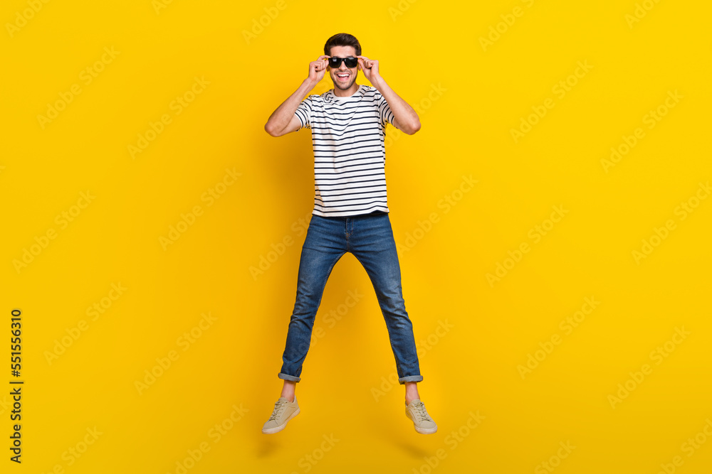 Full length photo of cool impressed man wear white t-shirt dark glasses jumping hight isolated yellow color background Full length photo of cool impressed man wear white t-shirt dark glasses jumping hight isolated yellow color background
