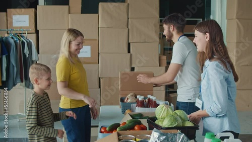 Friendly Volunteer Giving Donation Box With Food to Woman and Her Son at Distribution or Refugee Assistance Center. The Concept of Social Aid. Internally Displaced Persons photo