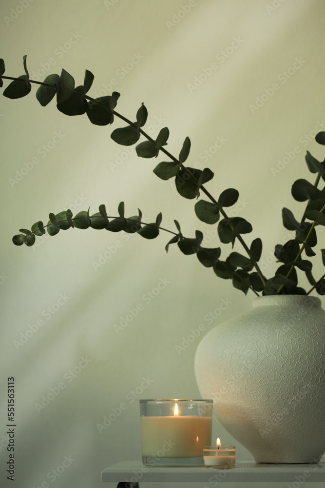 Burning candle, Leaf eucalyptus bouquet in bowl on beige interior. Selective soft focus. Minimalist still life. Light and shadow copy space background.