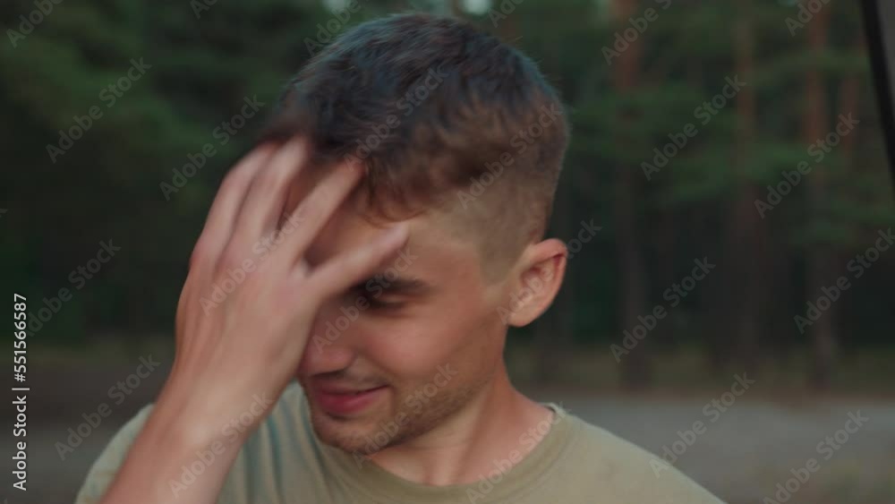 Portrait of young smiling guy who stands against the background of the forest and straightens his hair with his hand Portrait of young smiling guy who stands against the background of the forest and straightens his hair with his hand