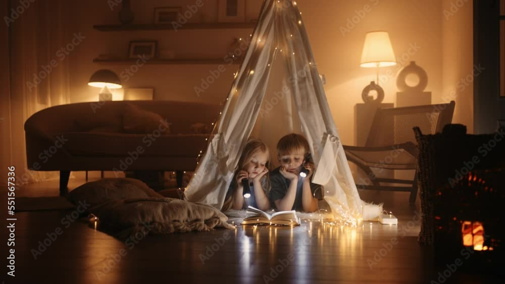 little siblings are playing in handmade wigwam from blanket in living room in winter night