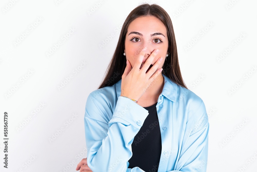 Emotional Young caucasian woman wearing blue overshirt over white background gasps from astonishment, covers opened mouth with palm, looks shocked at camera. Emotional Young caucasian woman wearing blue overshirt over white background gasps from astonishment, covers opened mouth with palm, looks shocked at camera.