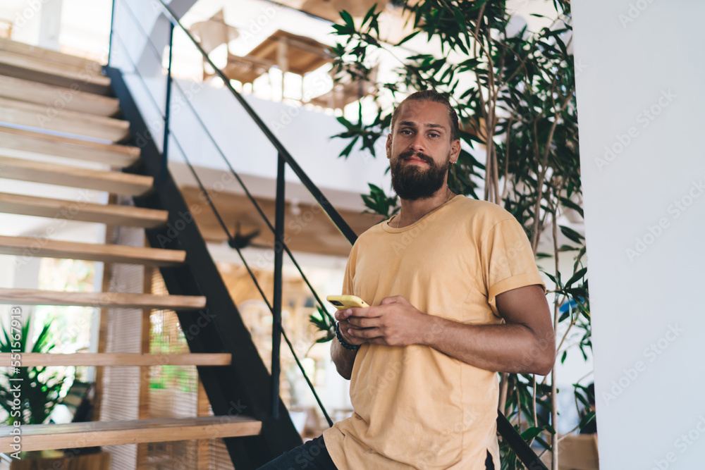 Confident bearded man with smartphone standing on stairs Confident bearded man with smartphone standing on stairs
