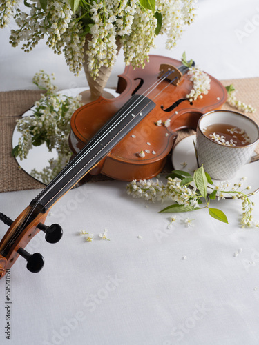 Artistic still life with a bouquet of bird cherries, a cup of tea and a violin. Vertical photo. Space for text.