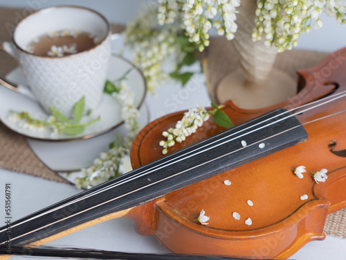 Artistic still life with a bouquet of bird cherries, a cup of tea and a violin. Horizontal photo.