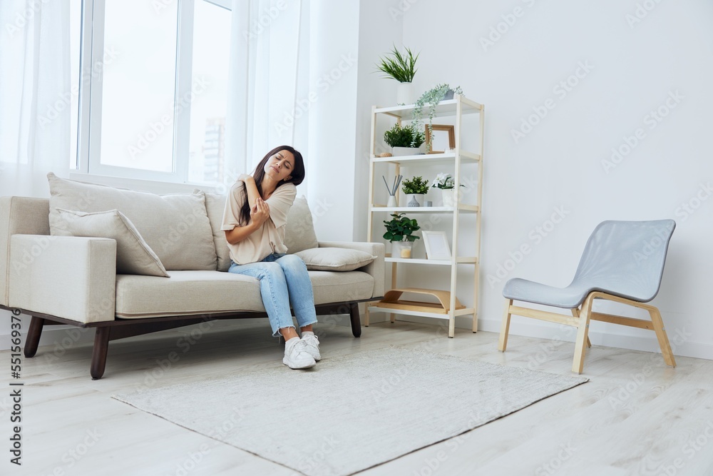 Woman sitting on sofa at home arm and shoulder pain, muscle sprain and joint pain, calcium problems in bones
