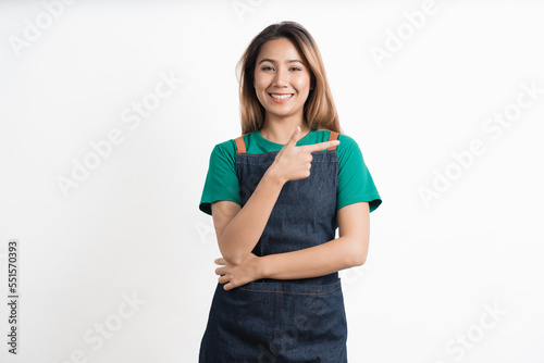 Young asian woman dressed in barista uniform pointing finger to the side on white background.
