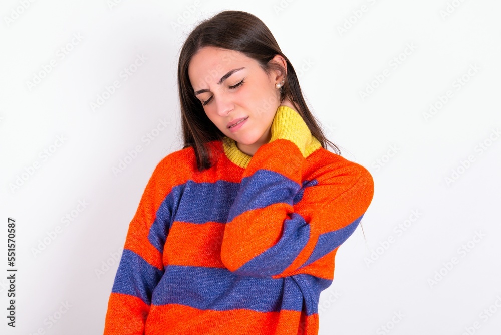 Young caucasian woman wearing colorful knitted sweater over white background Suffering of neck ache injury, touching neck with hand, muscular pain Young caucasian woman wearing colorful knitted sweater over white background Suffering of neck ache injury, touching neck with hand, muscular pain