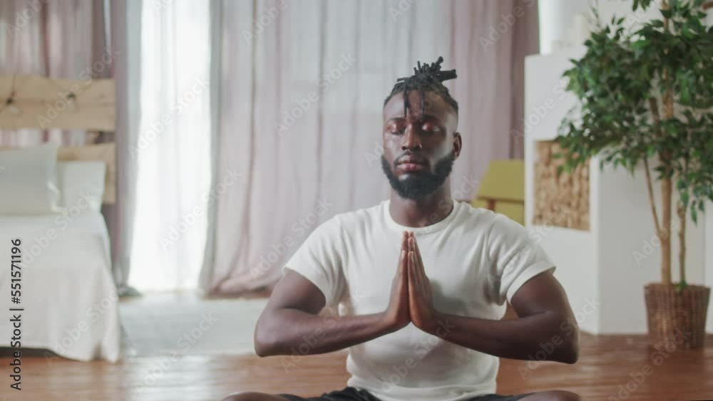 Young Beginer African American man in sporstwear practicing yoga on red fitness mat in living room. Close Up Prtrait Sporty male sit on mat in lotus position in living room. Healthcare and exercise Young Beginer African American man in sporstwear practicing yoga on red fitness mat in living room. Close Up Prtrait Sporty male sit on mat in lotus position in living room. Healthcare and exercise