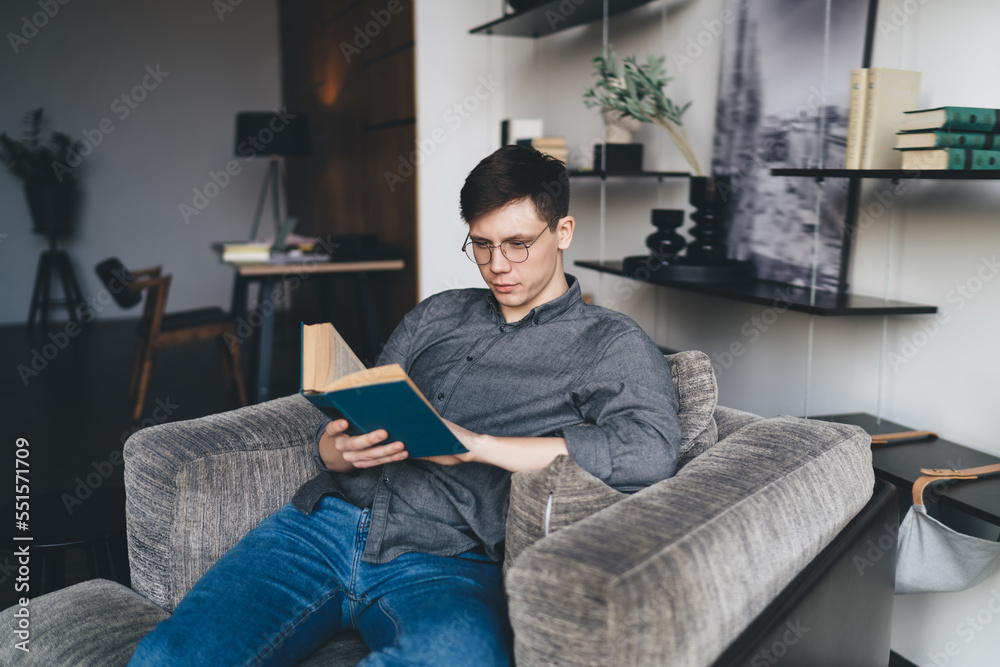 Focused young man reading book in living room at home